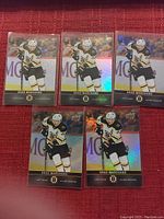 Five Upper Deck hockey cards featuring Brad Marchand in Boston Bruins white and black uniform with holographic accents shown on red background.