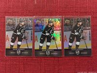 Three Upper Deck Drew Doughty hockey cards displayed on a red textured surface, two standard cards flanking one holographic card.