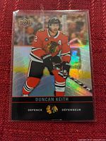 Holographic Upper Deck Duncan Keith hockey card in Chicago Blackhawks uniform shown on red fabric background.