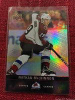 Holographic Upper Deck trading card showing Nathan MacKinnon in Avalanche white jersey in action with stick.