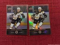 Two Upper Deck Patrice Bergeron Boston Bruins hockey cards shown side by side on a red surface, both cards holographic and in protective sleeves.