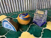 Three items showcased together on green and yellow tile surface: blue agate stone, round glass paperweight, clear stacked glass pieces.