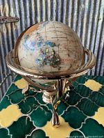 Overview of globe showing brass-tone metal base with three legs and colorful globe inset details of Oceania and surrounding areas.