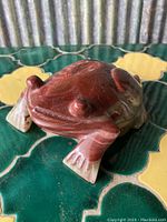 Front angle view of the polished solid onyx toad figurine placed on a green and yellow tray.