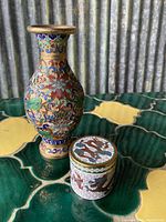 Photo showing both cloisonné pieces, the tall vase and the small trinket box side by side on a green and yellow tiled surface.