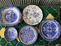 Five blue and white plates arranged on green tile surface, showing variety of traditional designs.