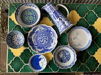 Top view of all 7 household ceramic items placed on a green and yellow tiled surface