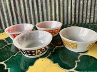 Four vintage Anchor Hocking bowls on a green and yellow surface, showing red, brown, orange, and yellow dice pip designs around the exterior.