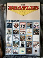 Full view of the framed Beatles discography litho print showing the title and album covers in a grid format.