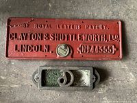 Vintage red cast iron license plate with raised text and number, along with cast iron bracket below it.