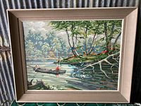 Full view of the framed paint by number painting depicting two people fishing in a boat on a river surrounded by forest.