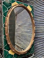 Front view of the vintage oval mirror showing gold ornate frame and clear reflective glass.
