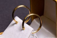Two 14k gold hoop earrings displayed on a white earring stand showcasing their front view.