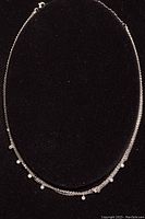 Full view of silver choker necklace held on black display, showing its delicate multi-strand chain design with stones.