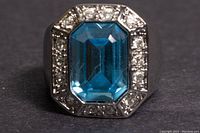 Front view of sterling silver ring with aquamarine center stone and surrounding cubic zirconia stones.