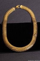 Wide view of the whole gold-toned choker necklace arranged flat on a black surface, showing chain mesh and clasp.