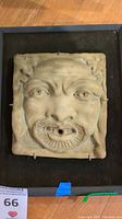 Front view of ceramic relief face tile secured in wooden frame with protective hooks