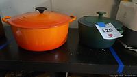 View of the orange LeCreuset Dutch oven and green Cuisinart Dutch oven with lids side by side on a table.