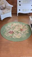 Full view of round green rug with floral center design in room setting with wicker furniture and dresser.