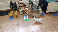 Group photo of various vintage animal figurines arranged on a floor showing variety including chickens, birds, ducklings, a deer/buck and cow creamers