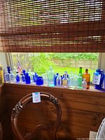 Full view of multiple glass bottles on windowsill in cobalt blue, clear, and amber shades, varying shapes and sizes.