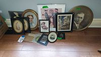 Wide shot showing the collection of framed vintage photos and prints arranged on the floor including oval and round frames, a Norman Rockwell print, and various portrait styles.