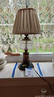 Full view of the vintage table lamp showing the shade, clear glass center, and ceramic base with electrical cord attached.