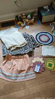 Overview of lot showing lace fabric, patterned blanket, two peach skirts, crocheted doilies/potholders, white linens and small animal figurines.