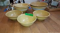 Seven vintage yellow ware mixing bowls arranged on a wooden floor showing yellow color with white stripes and varying sizes.