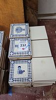 Stack of ceramic tiles including decorative and plain tiles with seller's lot number tag