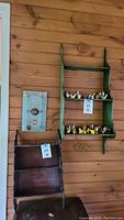 Green painted wooden shelf mounted on wall with small decorative figurines, next to dark wood shelf and blue wall panel.