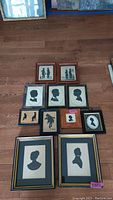 Collection of 12 framed silhouette portrait artworks laid out on wooden floor, showing a variety of frame styles and sizes.