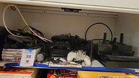 Photo showing Nintendo Wii, game cases including Mario & Sonic and Just Dance 4, various wired and wireless controllers and cables spread on a shelf.