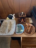View of entire lot on a wooden table including wooden multi-pipe holder with pipes, two distinct Mid-Century Modern style ashtrays, black round object, and white ceramic bird figurine.