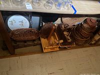 Photo showing wicker baskets, wooden trays, and stacked crab mallets beneath table.
