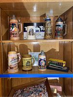 Shelf with eight beer steins, three on top shelf, five on bottom shelf plus collectible bus model on bottom shelf