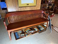 Front view of wooden bench showing the full length with spindle backrest and curved armrests.