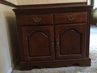 Front view of the Broyhill wooden server cabinet showing two drawers and two paneled doors with brass handles. Cabinet door arches and decorative molding visible.