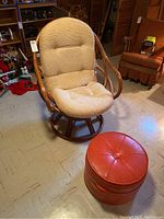 View of the swivel chair with beige cushioned seat and round red hassock ottoman on linoleum floor in basement setting.