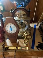 Photo of three clocks on wood surface with visible cords and wood-paneled background