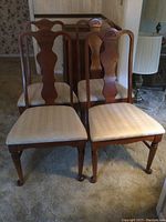 Four wooden dining chairs arranged in room, showing carved backs and upholstered seats with visible stains.