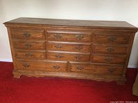 Full view of wooden dresser showing nine drawers, wood grain finish, and scalloped base