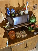 Bird, child and elephant figurines, along with Turkey candy dish, cabbage bowl and plate and sea shell jewelry boxes arranged on and around wooden furniture