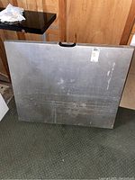 Photo of folded metal folding table showing the top surface with handle and visible wear marks.