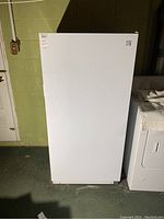 Front view of closed white upright freezer against basement wall