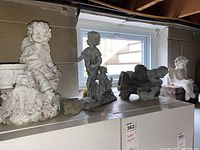 Four garden figurines on a shelf near a window in a basement showing angel and child themes with dogs.