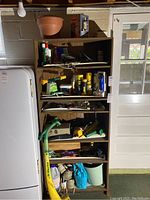 Shelf with various gardening supplies including chemical bottles, gloves, hand tools, and the Electralite weed eater