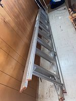 Full length view of the aluminum ladder leaning against a wood-paneled wall, showing the whole structure and rungs.