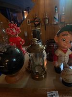 Front view of bowling ball decanter, ceramic softball player figurine, novelty candle holder, and other items on a wooden surface.