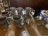 Wide view showing all pewter and metal cups, tankards, and bowl on table.